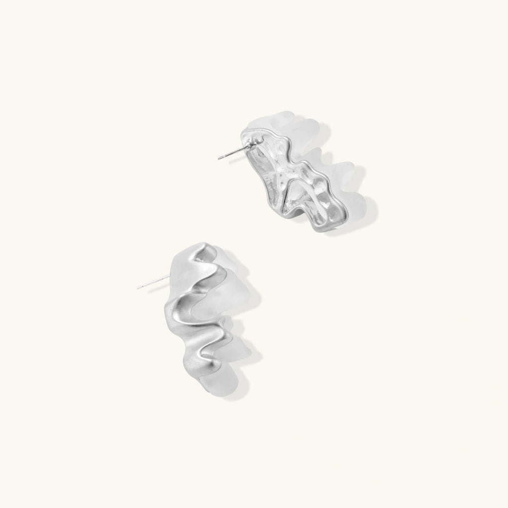 Pair of silver-toned sculptural earrings with flowing abstract forms and stud backs against white background.