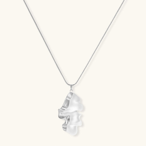 Modern sculptural pendant necklace with twisted metallic design on delicate silver chain against neutral background.